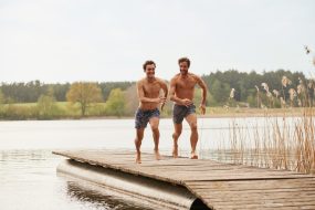 Zwei Männer liefern sich in Badehosen ein Wettrennen auf einem Badesteg.