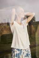 Frau steht mit genießerischem Gesichtsausdruck in Loungewear am Fenster.