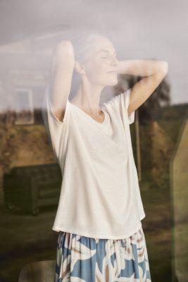 Frau steht mit genießerischem Gesichtsausdruck in Loungewear am Fenster.
