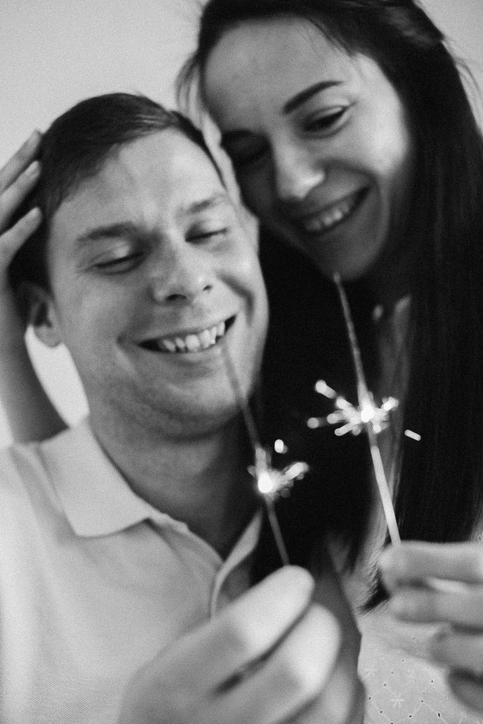 Silvester zu zweit - das kann sehr romantisch sein. Hier zu sehen ist ein Paar mit Wunderkerzen, beide lachen.